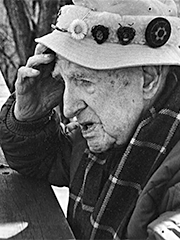 my grandfather as an old man wearing a scarf with rectangles and a hat decorated with discs