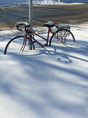 Bicycle in snow, with shadows forming bent circles with the wheels.  