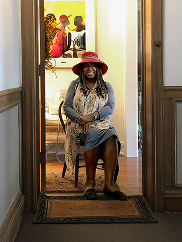 smiling lady in red hat sitting inside her open apartment door