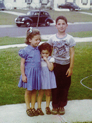 Two girls and a boy with old car and houses (my sister, me, by brother)