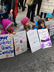 four little girls sitting on a curb with signs