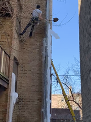 man repelling on wall to knock ice off drain with a shovel