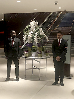 Men in suits standing by flowers in front of escalator