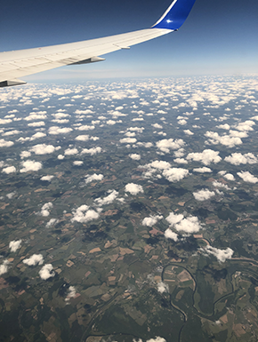 Plane wing above puffy little clouds over rural scene
